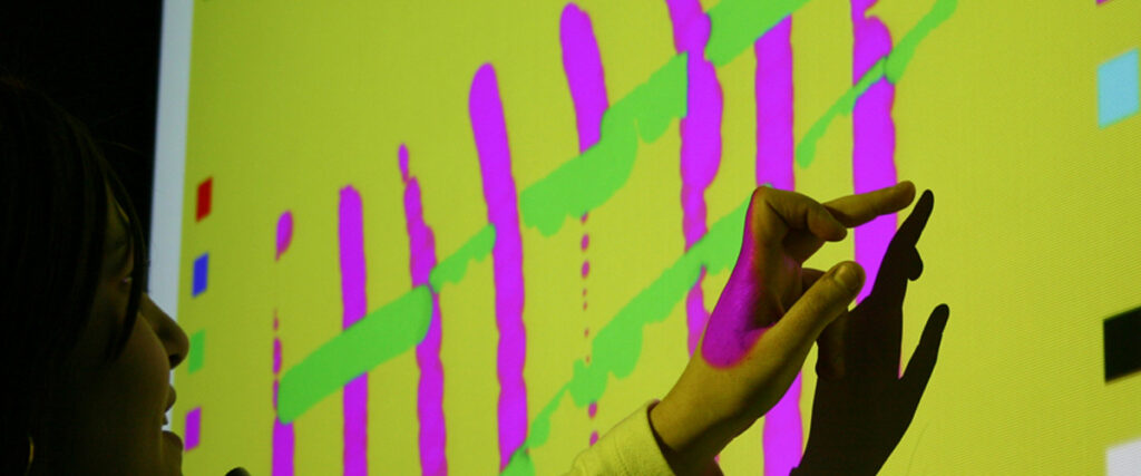 A person engaging with a brightly colored touchscreen displaying abstract patterns in green and pink on a yellow background, framed as if part of a pitch deck. The screen also features small blue squares and other colored shapes. Their hand is against the screen, casting a shadow.
