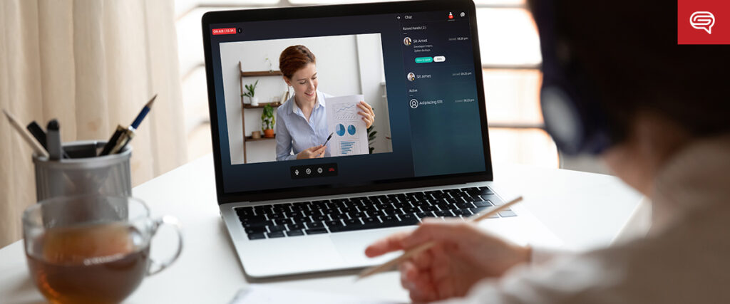 A person participates in a video call on a laptop. The screen shows another individual presenting a report with charts using PowerPoint. A cup of tea, a pen in a holder, and a notebook are on the desk. The person appears to be taking notes during the presentation.