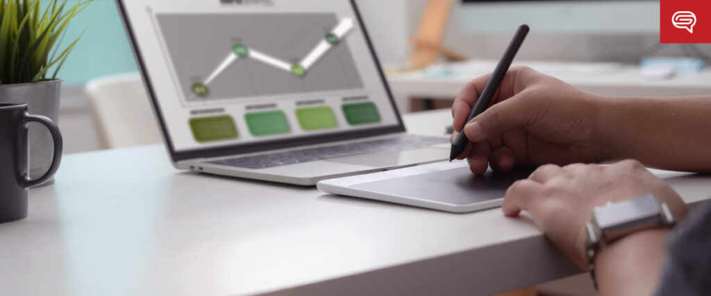 A person uses a stylus on a digital drawing pad at a white desk. A laptop displaying a line graph and a small potted plant are in the background. The person wears a smartwatch while working on their pitch deck. In the top right corner, there's a red icon with white speech bubbles.