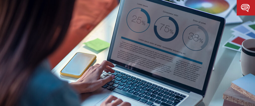 A person types on a laptop displaying data visualization graphics, including three circular charts labeled with percentages of 25%, 75%, and 38%. The workspace includes sticky notes, papers, a mobile phone on the desk, and an open pitch deck ready for presentation.