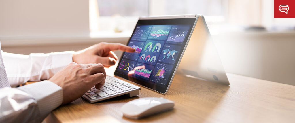 A person operating a tablet laptop in tent mode on a wooden desk, analyzing various financial and statistical graphs displayed on the screen. A wireless keyboard and mouse are also on the desk. Bright natural light filters through a window in the background, creating an ideal setting for reviewing a PowerPoint slide template.