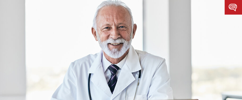 A smiling elderly male doctor with white hair and beard is wearing a white coat and a stethoscope around his neck. He stands in a bright room with large windows behind him, reminiscent of the clean aesthetics often used for animations in pitch decks.
