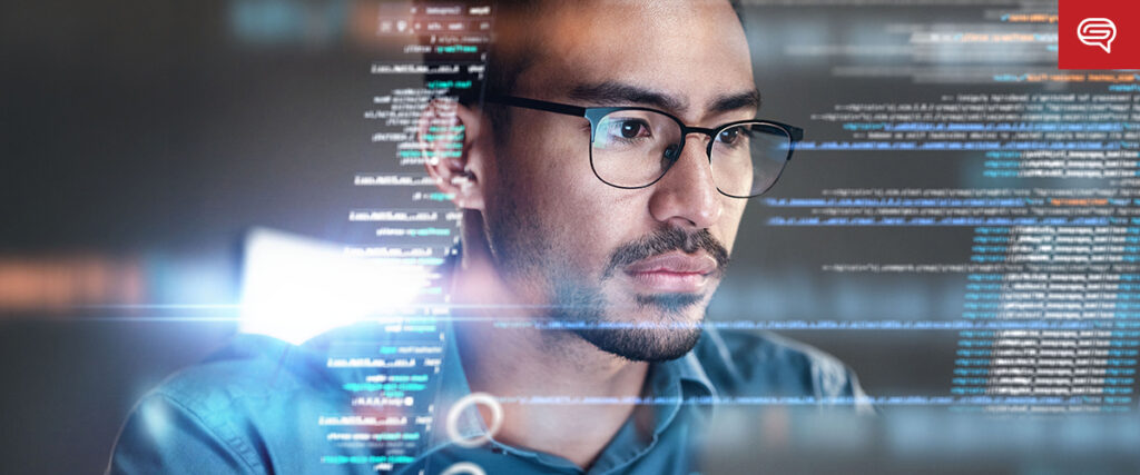 A man wearing glasses focuses intently on a computer screen, immersed in preparing a quality earnings report. Reflected code and digital elements overlay part of the image, suggesting he is meticulously programming the data presentation. The background is blurred, emphasizing the man and his task.
