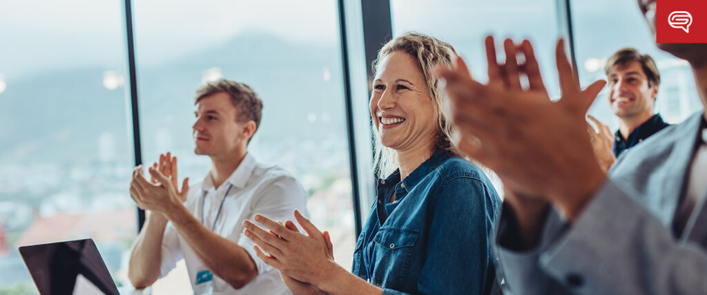 A group of people is sitting and clapping, looking happy and engaged as they enjoy the seed funding round presentations. The setting appears to be a conference or meeting room with large windows in the background.