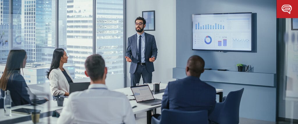 A man in a suit presents a data report to four colleagues in a modern conference room. The client experience slide is displayed on a large screen, showing various graphs and charts. Large windows reveal a cityscape in the background, perfect for consulting firms to discuss insights.